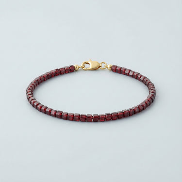A 3mm faceted Garnet cube bead bracelet featuring deep burgundy tones and a high-polish gold lobster clasp, displayed against a light grey background.
