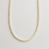 A delicate strand of small white freshwater pearls displayed in a U-shape against a neutral background.

