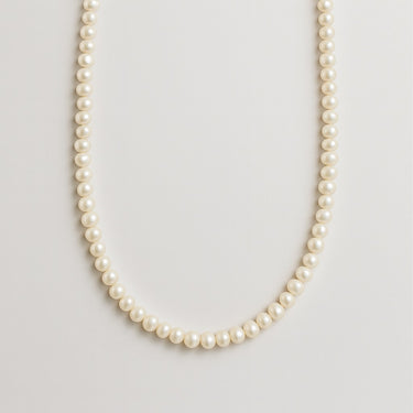 A delicate strand of small white freshwater pearls displayed in a U-shape against a neutral background.
