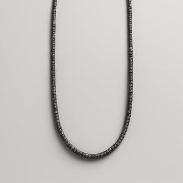 A single strand of 4mm porous black lava heishi beads displayed in a U-shape against a neutral light grey background.
