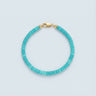 A 4mm sky-blue turquoise heishi bead bracelet with a high-polish gold lobster clasp, displayed against a light grey background.
