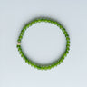 A slim 4mm green jade bead bracelet featuring a single 14K gold-filled accent bead, displayed against a light grey background.
