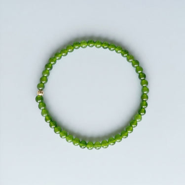 A slim 4mm green jade bead bracelet featuring a single 14K gold-filled accent bead, displayed against a light grey background.
