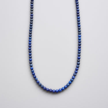 A strand of 4mm deep blue lapis lazuli beads displayed in a U-shape against a bright white background.
