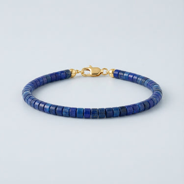 A 4mm Lapis Lazuli heishi bead bracelet with a high-polish gold lobster clasp, displayed against a light grey background.
