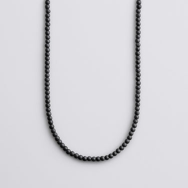 A strand of 4mm matte black onyx beads displayed in a U-shape against a neutral light grey background.
