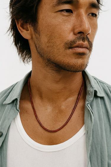 Side view of a model wearing a 4mm red agate heshi necklace styled with a light blue button-down shirt.
