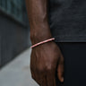 A close-up of a male model's wrist showcasing the muted pink tones and low-profile fit of a 4mm Rhodonite heishi bead bracelet.

