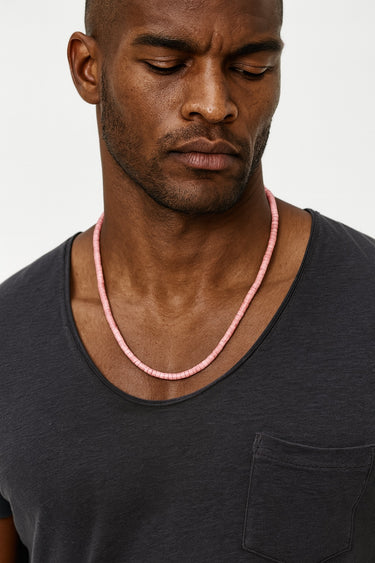 A male model wearing a black v-neck t-shirt showcasing the muted rose tones and textured drape of a 4mm Rhodonite heishi necklace.

