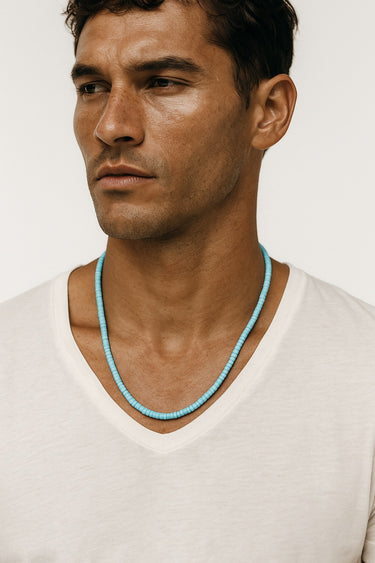 Front view of a model wearing a 4mm turquoise heshi necklace styled with a white v-neck t-shirt.

