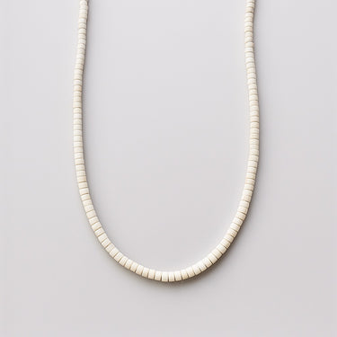 A single strand of 4mm crisp white turquoise heishi beads displayed in a U-shape against a neutral light grey background.
