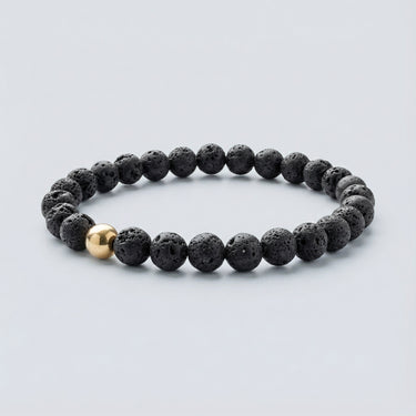 A 6mm Black Lava round bead bracelet featuring a porous volcanic texture and a single 14K gold-filled accent bead.
