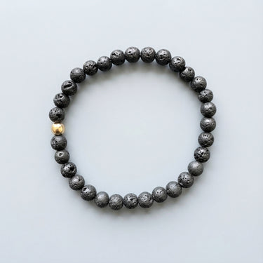 A top-down view of a 6mm Black Lava bead bracelet, highlighting the tactile matte surface and the polished gold accent bead.
