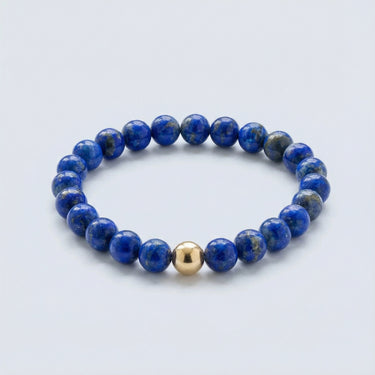 An angled editorial view of a 6mm Blue Lapis Lazuli bead bracelet highlighting the polished gold-filled accent bead and natural pyrite flecks.
