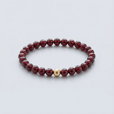 An angled editorial view of a 6mm Garnet bead bracelet highlighting the polished gold-filled accent bead and natural stone depth.
