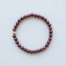 A 6mm Garnet round bead bracelet featuring deep wine-red stones and a single 14K gold-filled accent bead, displayed against a light grey background.
