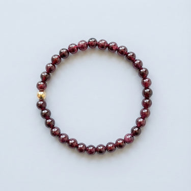 A 6mm Garnet round bead bracelet featuring deep wine-red stones and a single 14K gold-filled accent bead, displayed against a light grey background.
