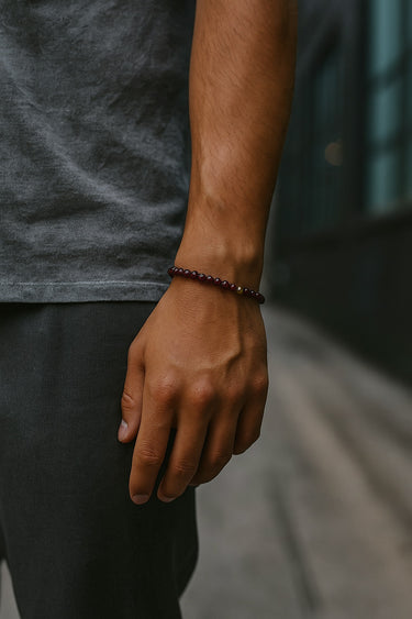 A close-up of a male model's wrist showcasing the rich, dark red hues and 6mm scale of a Garnet bead bracelet.
