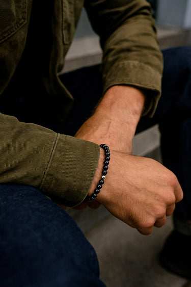 A lifestyle shot of a male model wearing a 6mm Gloss Black Onyx bracelet, showcasing its deep obsidian color and high-shine finish.
