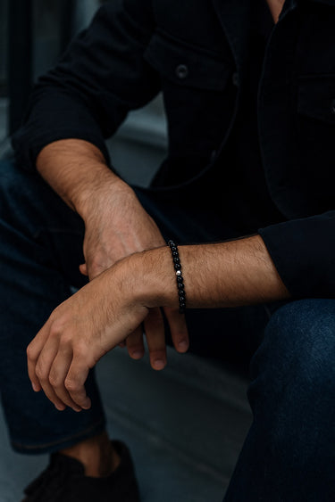 A lifestyle shot of a male model wearing a 6mm Gloss Black Onyx bracelet, showcasing its deep obsidian color and high-shine finish.
