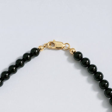 Close-up of a men’s necklace with 6mm gloss black onyx beads and a polished 14K gold-filled lobster clasp.