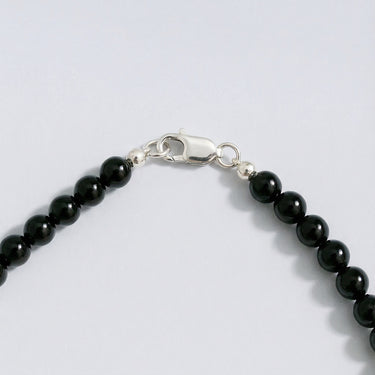 Close-up of gloss black onyx beads with sterling silver accent beads and lobster clasp detail on a white background.