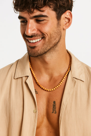 A smiling man in a tan short-sleeve button-down shirt wearing a single strand of 6mm golden sandalwood beads.
