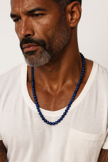 A male model wearing a white t-shirt showcasing the deep, vibrant blue of a 6mm Grade A Lapis Lazuli beaded necklace.
