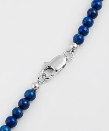 Close-up of lapis lazuli gemstone beads with sterling silver accent beads and lobster clasp detail on a white background.
