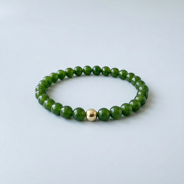 An angled editorial view of a 6mm jade bead bracelet highlighting the polished gold-filled accent bead.

