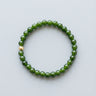 A 6mm green jade bead bracelet featuring a single 14K gold-filled accent bead, displayed against a light grey background.
