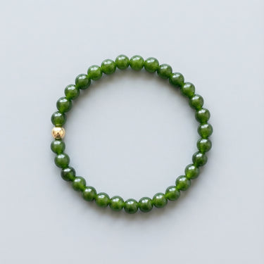 A 6mm green jade bead bracelet featuring a single 14K gold-filled accent bead, displayed against a light grey background.
