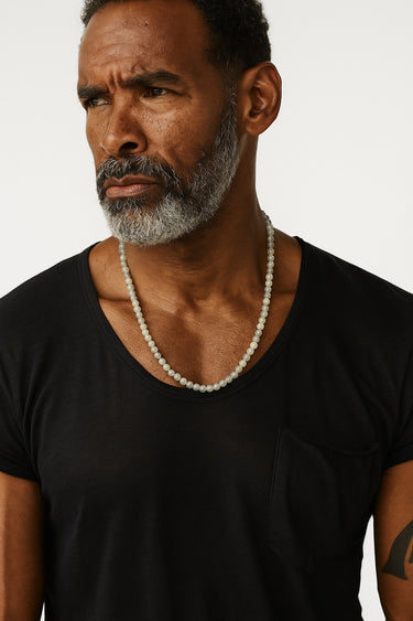 A male model wearing a black v-neck t-shirt showcasing the blue-grey flashes of a 6mm labradorite gemstone necklace.
