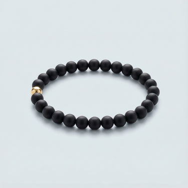An angled editorial view of a 6mm matte black onyx bead bracelet showcasing the contrast between the muted stone and polished gold accent.
