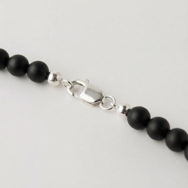 Men’s 6mm matte black onyx bead necklace featuring smooth natural black gemstone beads with sterling silver accent beads and lobster clasp detail on a white background.