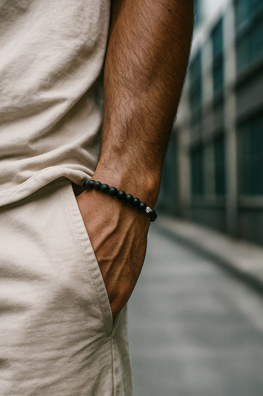 A close-up of a male model's wrist showcasing a 6mm matte black onyx bracelet paired with neutral-toned linen trousers.
