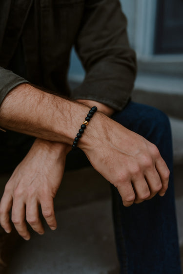A lifestyle shot of a male model wearing a 6mm matte black onyx bracelet, highlighting its velvety texture and slim, architectural profile.
