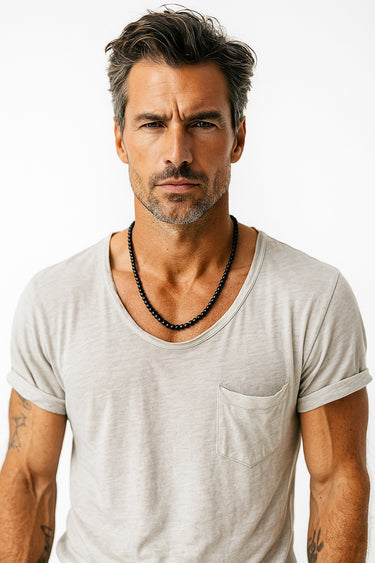 A male model wearing a light grey v-neck t-shirt showcasing the substantial drape of 6mm matte black onyx beads.
