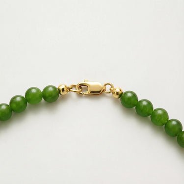 Close-up of natural green jade beads with polished 14k gold-filled accent beads and lobster clasp detail on a white background.