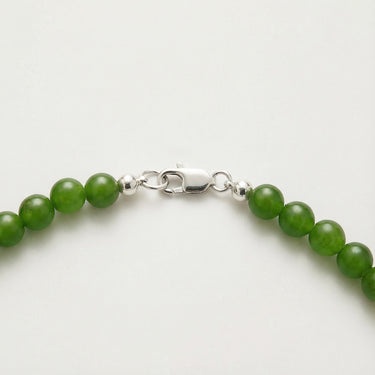 Close-up of natural green jade beads with polished sterling silver accent beads and lobster clasp detail on a white background.