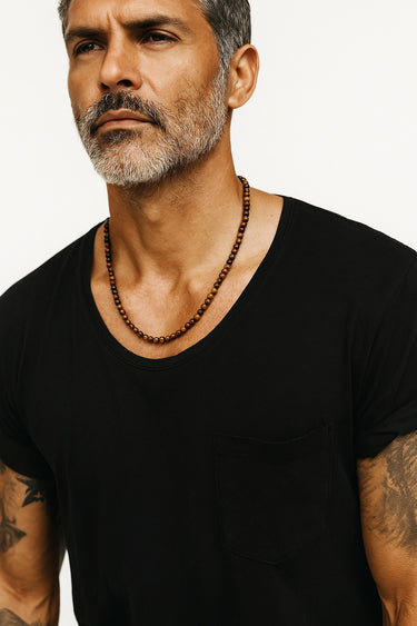 A male model wearing a black t-shirt showcasing the warm, golden-brown chatoyancy of a 6mm Tiger's Eye beaded necklace.
