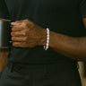 A close-up of a male model's wrist showcasing the organic texture and high luster of a 7-8mm white baroque pearl bracelet while holding a black mug.
