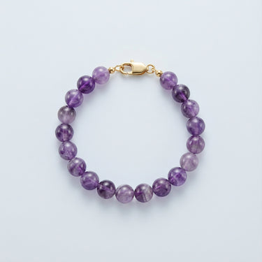 An 8mm Amethyst round bead bracelet with a high-polish gold lobster clasp, highlighting the natural color gradients of the gemstone.
