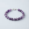 An 8mm Amethyst round bead bracelet featuring vibrant purple tones and a high-polish silver lobster clasp, displayed against a light grey background.
