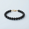 An 8mm Black Lava round bead bracelet featuring a porous volcanic texture and a high-polish gold lobster clasp, displayed against a light grey background.
