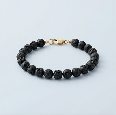 An 8mm Black Lava round bead bracelet featuring a porous volcanic texture and a high-polish gold lobster clasp, displayed against a light grey background.
