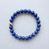 An 8mm deep blue Lapis Lazuli round bead bracelet featuring a single 14K gold-filled accent bead, displayed against a light grey background.
