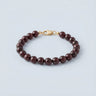 An 8mm Garnet round bead bracelet featuring deep wine-red stones and a high-polish gold lobster clasp, displayed against a light grey background.
