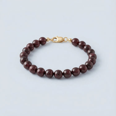 An 8mm Garnet round bead bracelet featuring deep wine-red stones and a high-polish gold lobster clasp, displayed against a light grey background.

