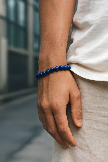 An editorial lifestyle shot of a male model wearing an 8mm Lapis Lazuli bracelet against neutral-toned clothing.
